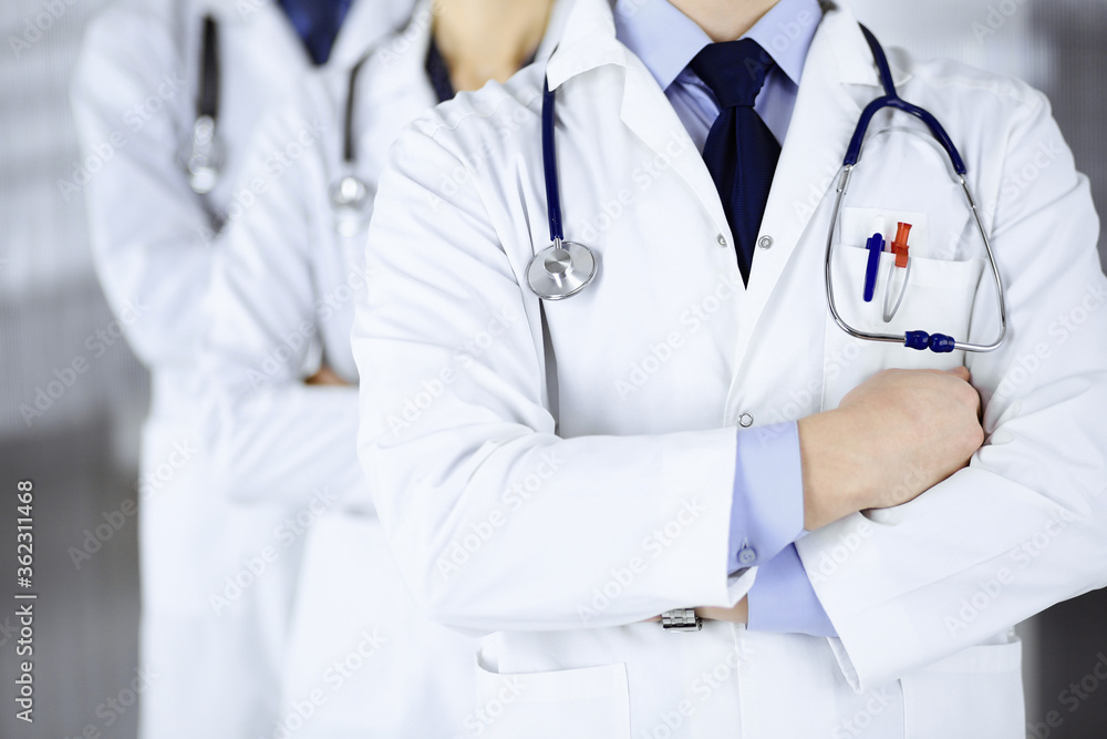Group of modern doctors standing as a team with crossed arms and stethoscopes in hospital office. Physicians ready to examine and help patients. Medical help, insurance in health care, best desease Group of modern doctors standing as a team with crossed arms and stethoscopes in hospital office. Physicians ready to examine and help patients. Medical help, insurance in health care, best desease
