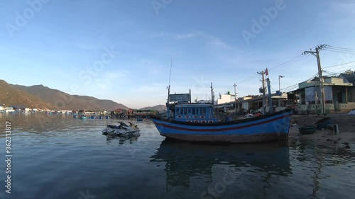 Small authentic Vietnamese blue boat docked by residential home in harbor with two personal watercrafts with mountain in background, Binh Hung island, Vietnam, handheld photo