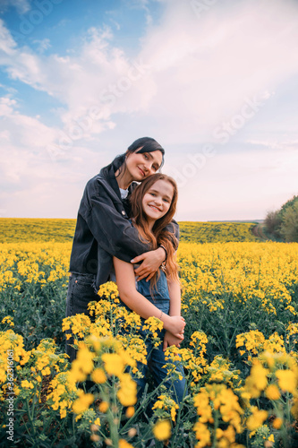 Portrait family photo mother tenderly lovingly hugs daughter. Woman brunette cute smiling. Redhaired girl laughs cheerfully. Backdrop scenic landscape flowering field blue sky. Yellow rapeseed flowers