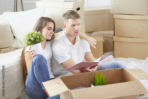 Portrait of happy couple looking at laptop computer together sitting in new house, surrounded with boxes © lenetsnikolai