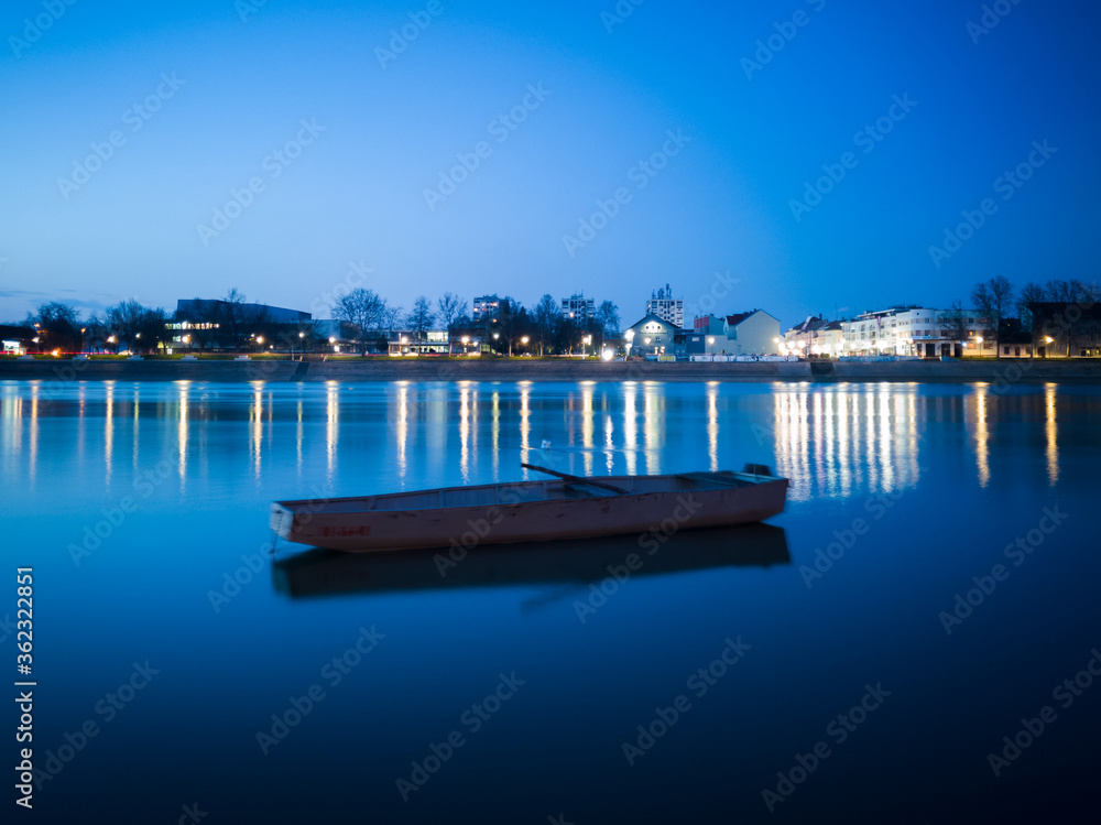 Naklejka premium Blue hour on Sava river, promenade in Slavonski Brod and blurred boat in front.