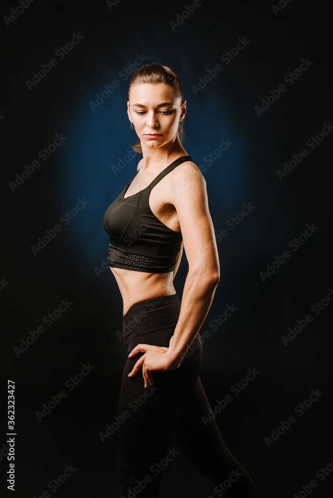 Slim fitness woman in black sport suit posing on black background