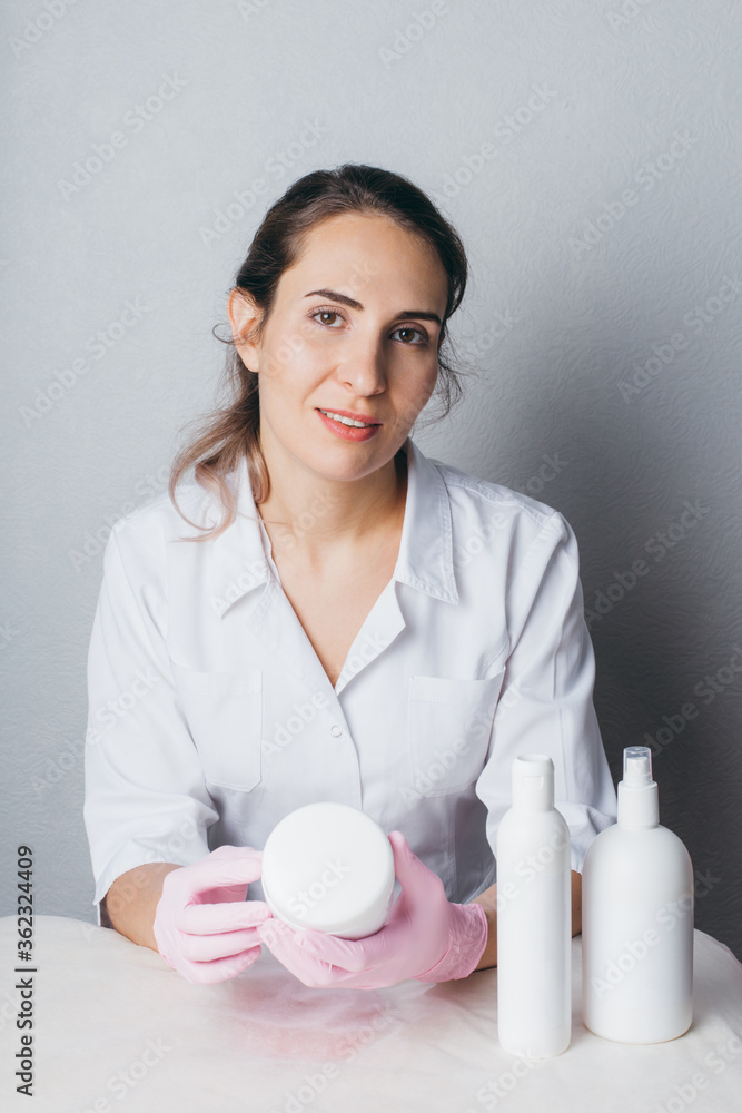 Beautician in white uniform and pink gloves holding a jar and bottle with cosmetic. Beautician in white uniform and pink gloves holding a jar and bottle with cosmetic.