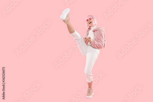 Women power! Full length shot of young energetic girl doing high kick in air while dancing, isolated on pink background photo
