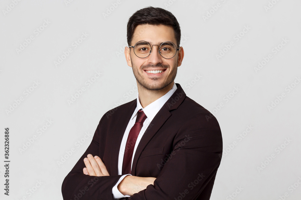 Smiling young businessman in burgundy suit, looking at camera with crossed arms, isolated on gray background Smiling young businessman in burgundy suit, looking at camera with crossed arms, isolated on gray background