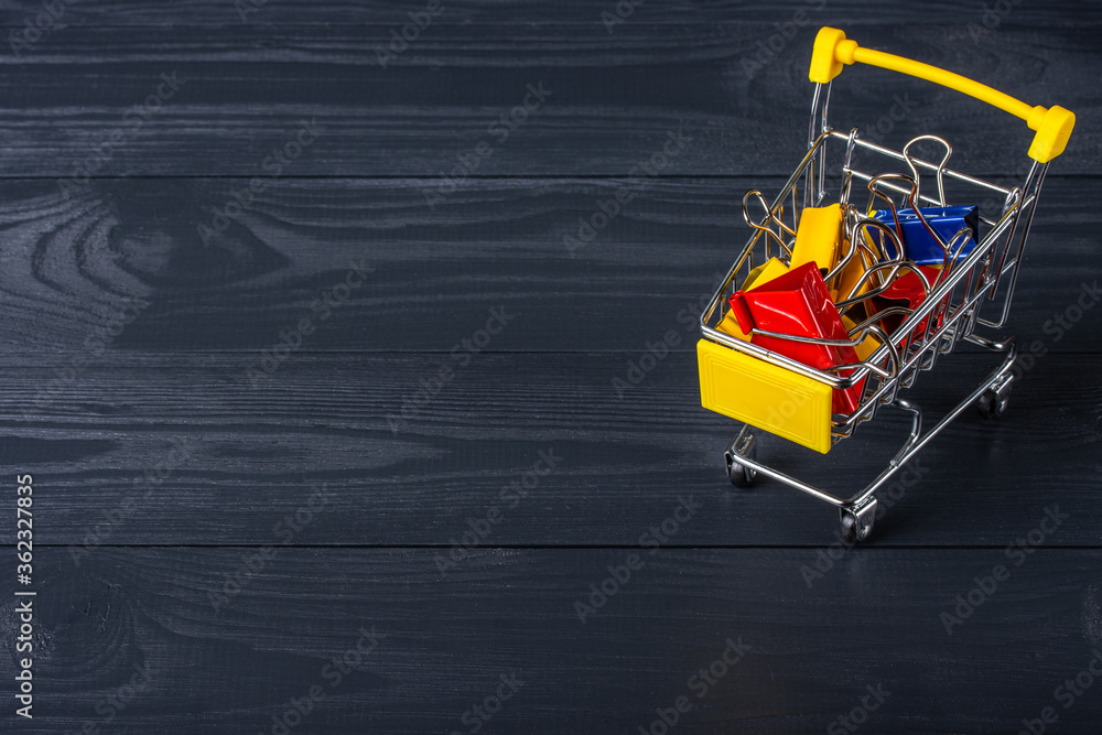 Naklejka premium Paper clips in shopping cart on a black wooden background