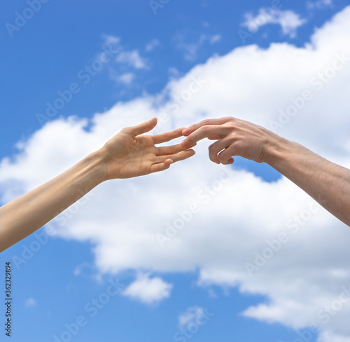 Male and female hand reach for each other and touch their fingers on a background of blue sky and white clouds. Lending a helping hand. Solidarity, compassion,and charity, rescue. Volunteer concept. © Serhii Khanas