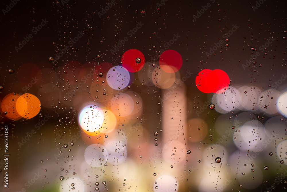 Raindrops on the window glass at night against the background of bokeh from the lights and Windows of the houses opposite