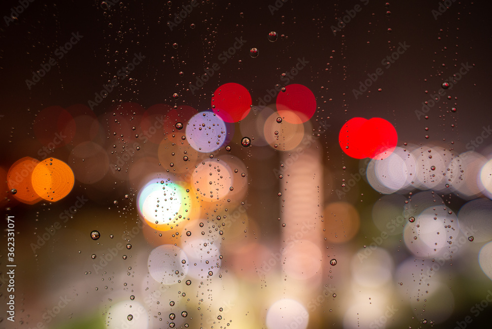 Raindrops on the window glass at night against the background of bokeh from the lights and Windows of the houses opposite