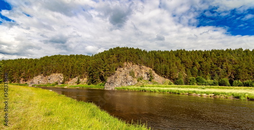 River in summer on the background of rocks, pines, blue sky and white clouds