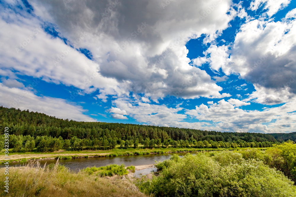 River in summer against forest on hills, blue sky and white clouds