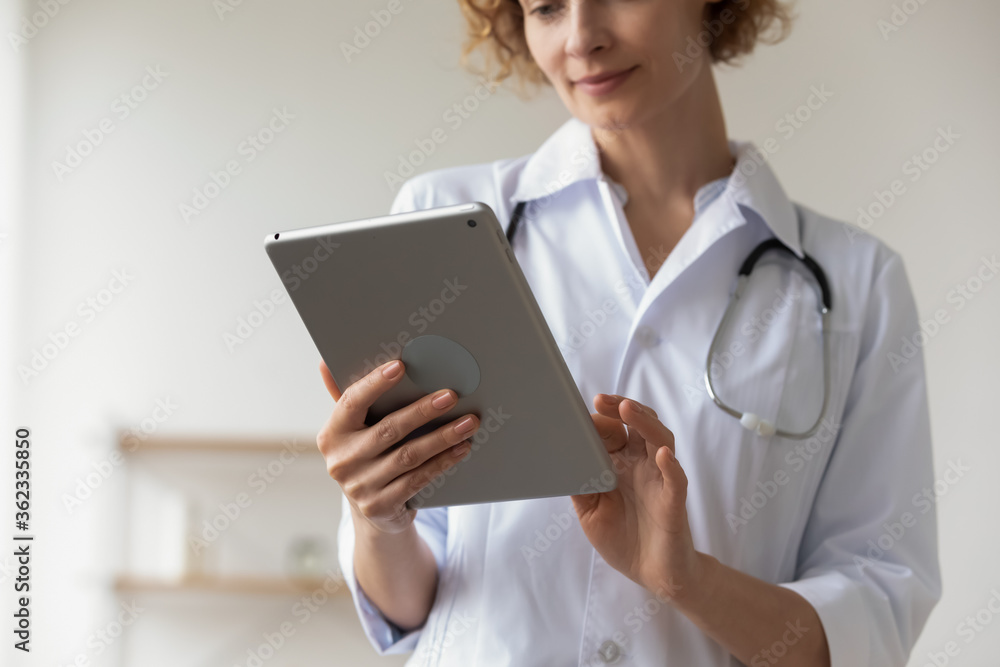 Crop close up of female doctor hold tablet fill patient medical history anamnesis online, woman nurse or GP use pad gadget, consult client on internet, browse results on device, technology concept Crop close up of female doctor hold tablet fill patient medical history anamnesis online, woman nurse or GP use pad gadget, consult client on internet, browse results on device, technology concept