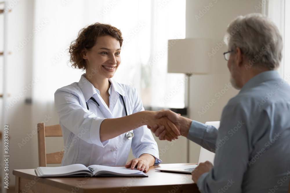 Smiling young female doctor shake hand of mature male patient at consultation in hospital, close health insurance deal, happy woman GP handshake senior man client, get acquainted greeting at meeting Smiling young female doctor shake hand of mature male patient at consultation in hospital, close health insurance deal, happy woman GP handshake senior man client, get acquainted greeting at meeting