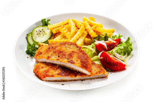 Breaded fried pork chop, French fries and vegetables on white background
