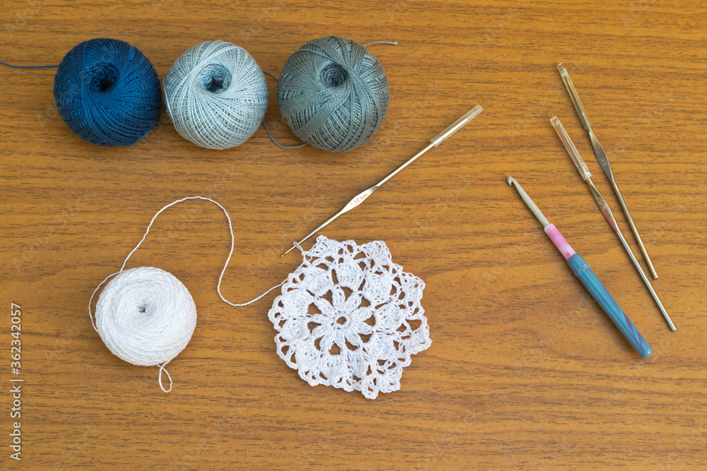 Crochet a lace white doily. Set of crochet hooks of different sizes and balls of cotton yarn on a wooden table. Needlework and knit concept. Flat lay, close-up, top view