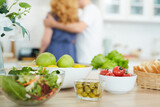 Close up of healthy food and snacks on kitchen counter with blurred silhouette of couple cooking in background, copy space