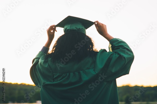 Canvas Print Young woman in a green academic dress holding a gown cap - the concept of gradua