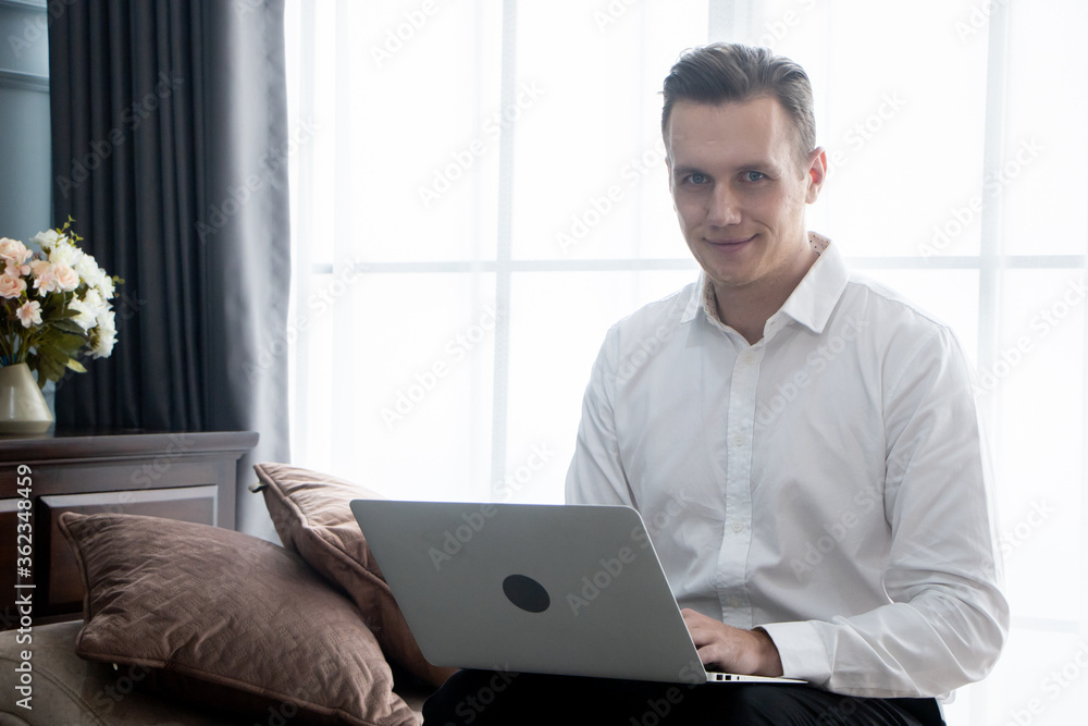 Smiling young man working on laptop, checking email in morning, writing message in social network.