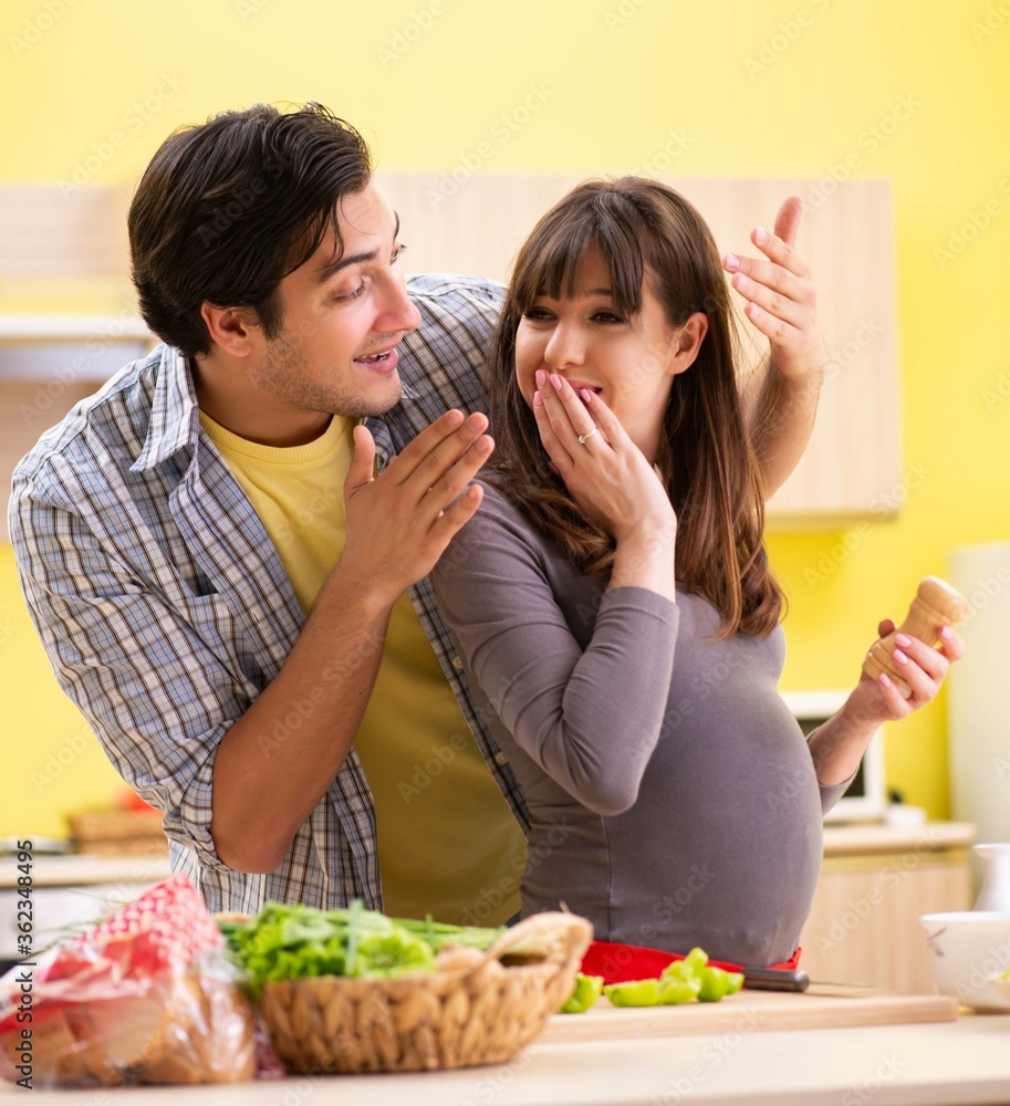 Man and pregnant woman preparing salad in kitchen