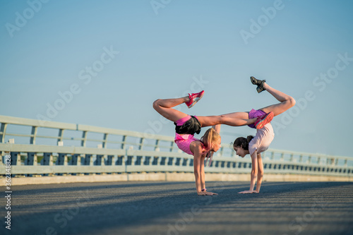 Two teenage girls perform an acrobatic element outdoors against a blue sky