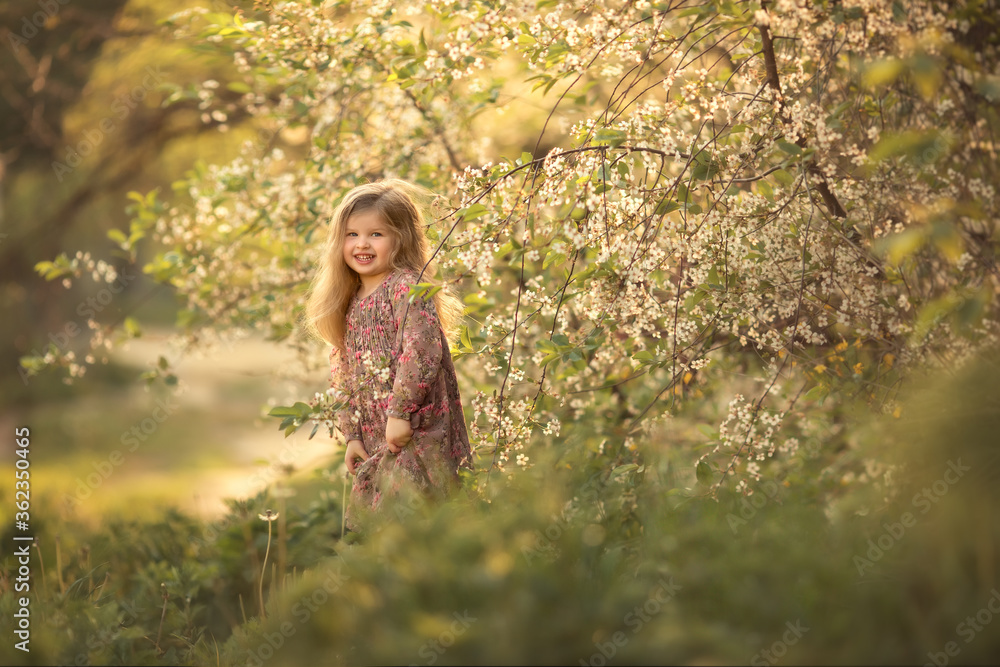 A little girl stands next to a large blooming spring tree. Image with selective focus. A little girl stands next to a large blooming spring tree. Image with selective focus.