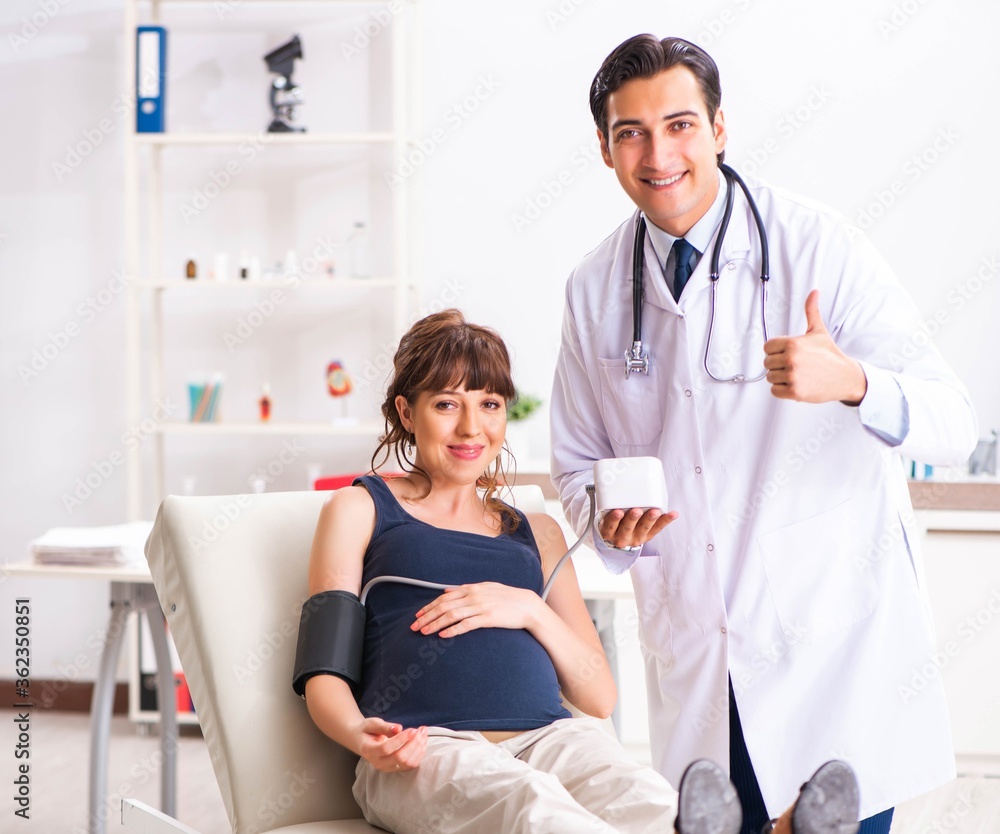 Fototapeta premium Young doctor checking pregnant woman's blood pressure