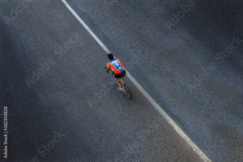 Lonely blurred cyclist or biker with shirt but without helmet on an asphalt road with only a white line that is diagonal in the photo. View from above
