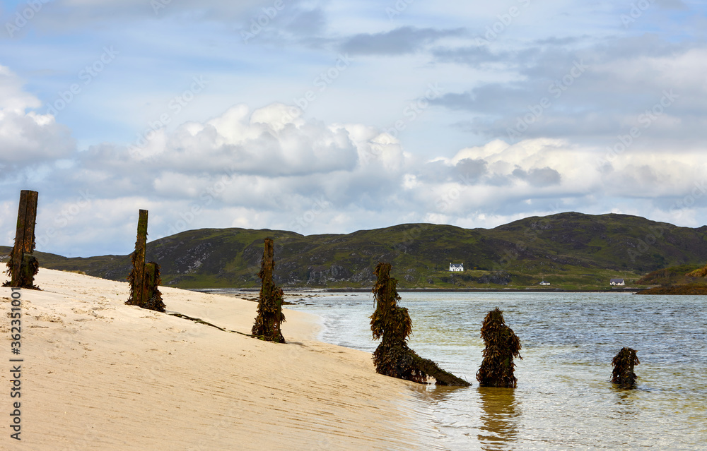 Large sandy beach on summers day Scottish Highlands Scotland with green hills sea water disappearing fence covered in seaweed and white cottages 