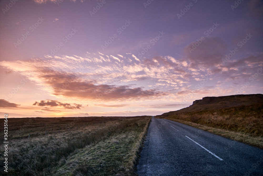 Road disappears over horizon into warm setting sun on isle of sky Scotland Scottish highlands 