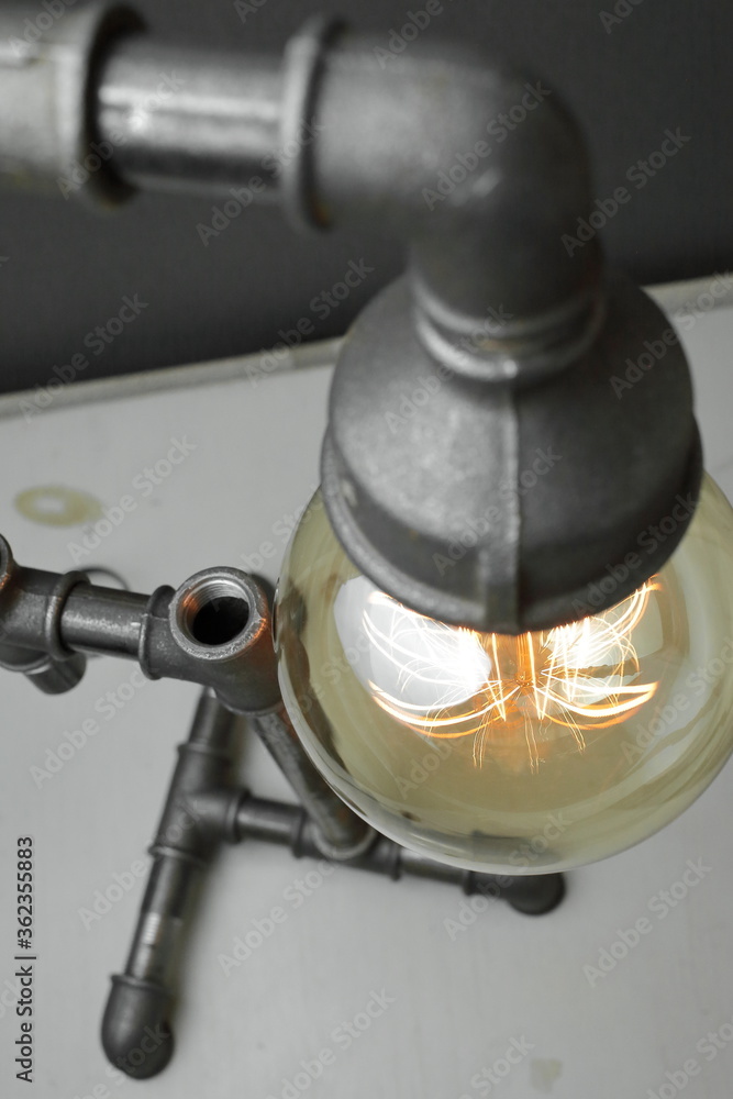 Retro lamp made of metal water pipes with an Edison lamp on a gray background. The concept is a good idea. Retro lamp made of metal water pipes with an Edison lamp on a gray background. The concept is a good idea.