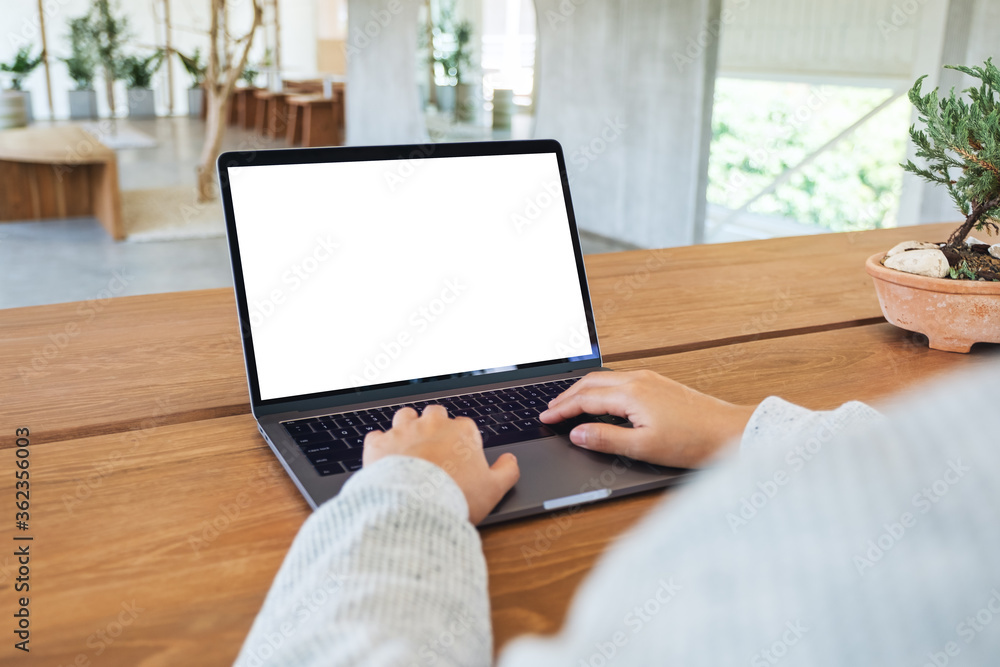 Fototapeta premium Mockup image of a woman using and typing on laptop computer keyboard with blank white desktop screen on wooden table