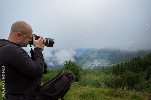 Male photographer taking a picture using professional DSLR while hiking in the Swiss Alps near Lauterbrunnen and Wengen in the Jungfrau Region on a foggy day. Switzerland