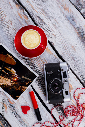 Flat lay hipster female accessories on white wood. Vintage photo camera with cup of coffee bead necklace and mascara. photo