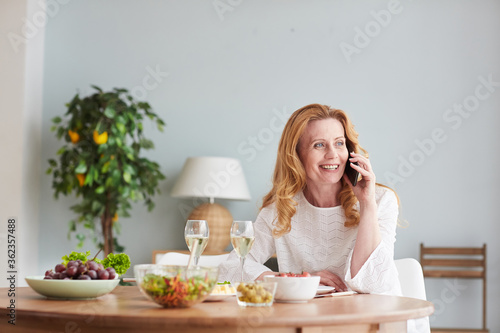 Portrait of elegant mature woman speaking by smartphone while enjoying dinner at home or cafe  copy space