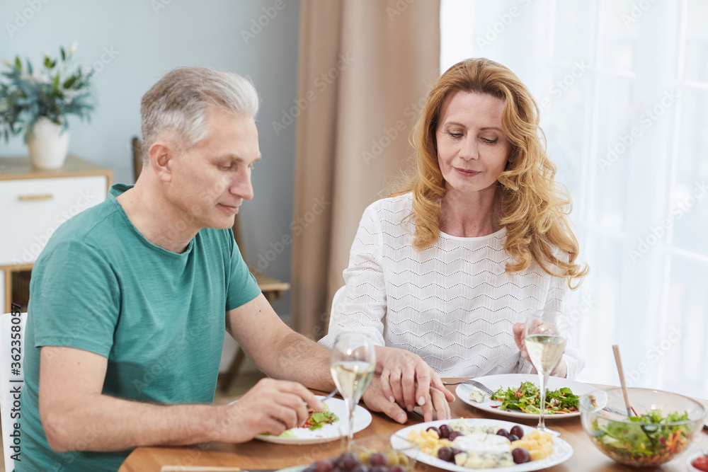 Portrait of modern mature couple holding hands while enjoying healthy dinner together at home, copy space