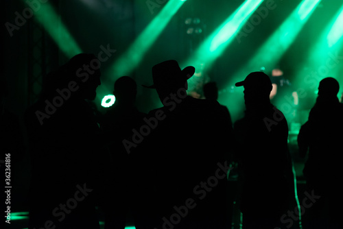 Blurred image of silhouette of raised arms, crowd of people in the front of bright stage lights at rock festival