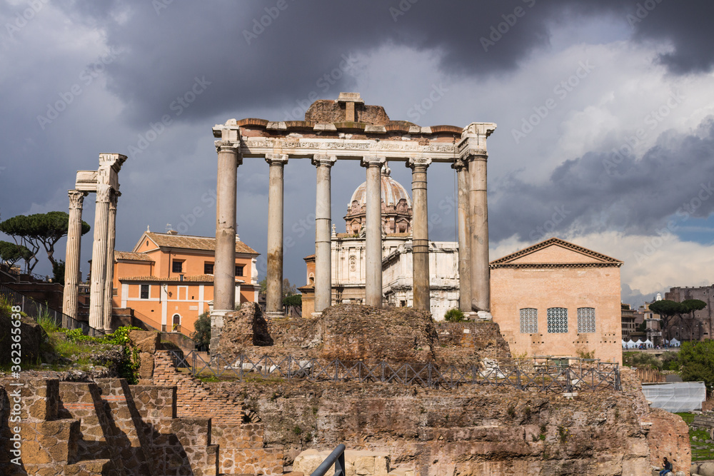 Roman forum in the sun against a dark, clouded sky. Ancient architecture and cityscape of historical Rome.