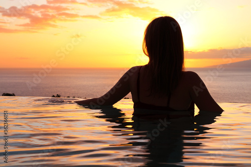 TENERIFE / SPAIN-12.03.19. A girl in a swimsuit with her hair down stands in the pool and looks at the sunset and the ocean.
