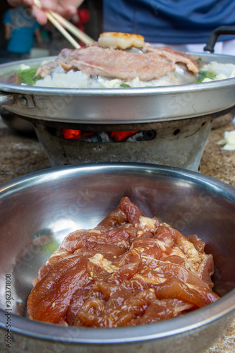 A raw pork in a bowl ready for grilling at Thai Barbecue style. A preparation of roasted meat with sauce of vegetable on Hot Pot - Mu Kratha, close up. photo