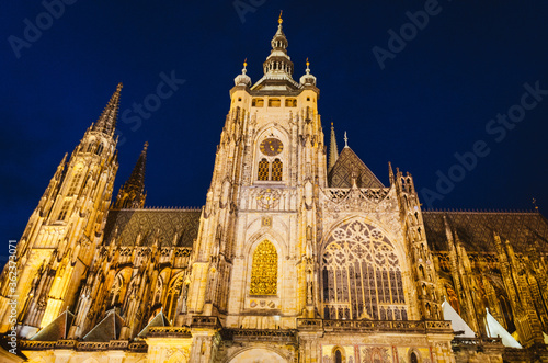 Dramatic view of the Prague Castle illuminated by warm yellow lights in a dark blue sky.