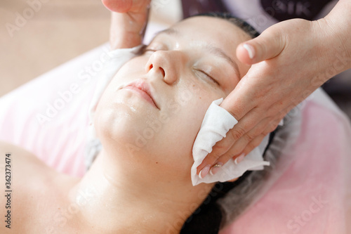 Female with healthy glow perfect smooth skin. Young woman getting spa treatment at beauty salon. Skincare concept. Hands of cosmetology specialist cleaning face with cosmetic cotton white pad.