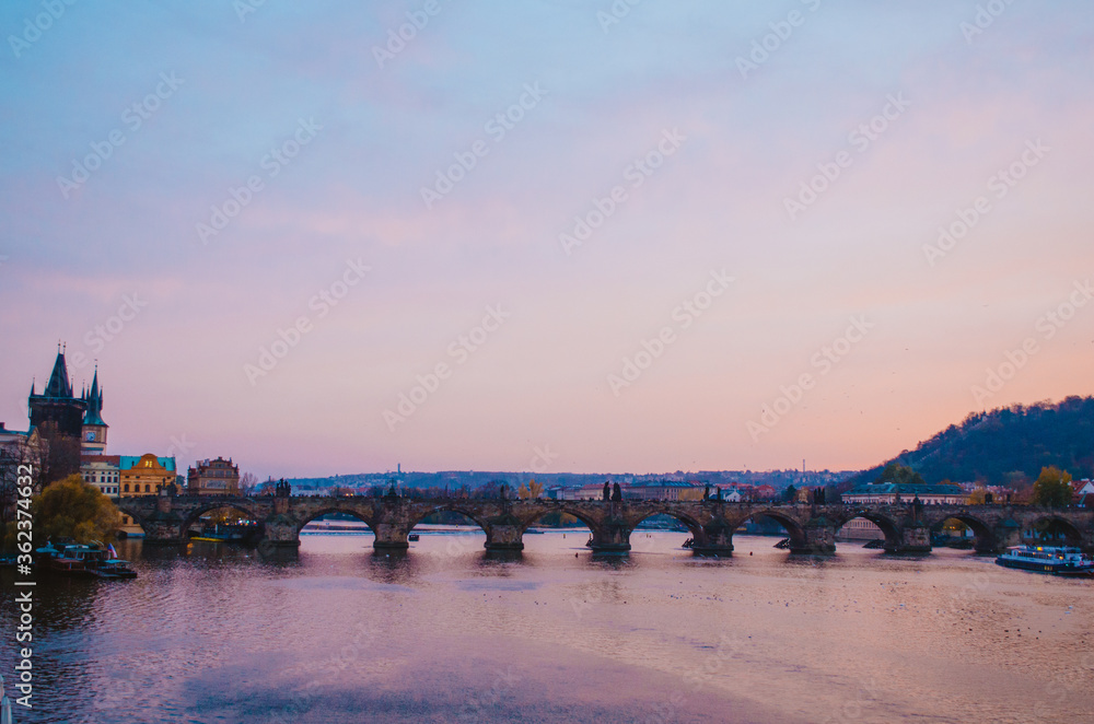 Sundown in the Vltava River with a view to Charles Bridge and a gradient of purple to pink colors reflecting from the sky.