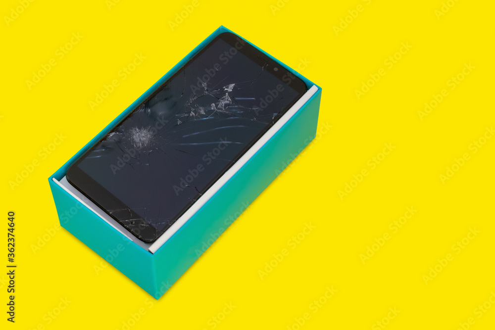 smartphone with a broken screen in a blue gift box on a yellow background smartphone with a broken screen in a blue gift box on a yellow background