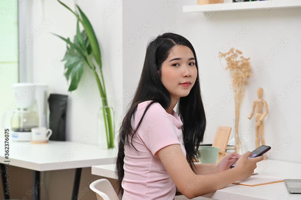A beautiful woman is using a smartphone while sitting at the white working desk. A beautiful woman is using a smartphone while sitting at the white working desk.