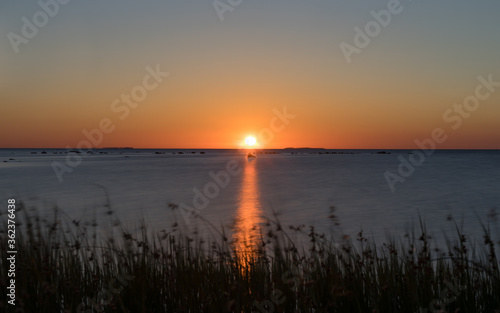 Orange sunset sky over Suur Strait. Nordic white night during Midsummer period. North coast of small Muhu island. Sun is just above the horizon, distinctive stripe over smooth water. Baltic sea.
