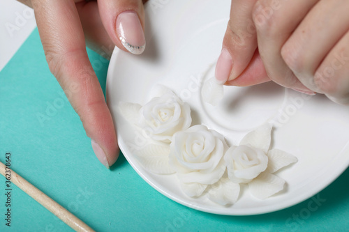 Roses with petals made of white polymer clay. A woman sticks them on a saucer. Crafts from polymer clay.
