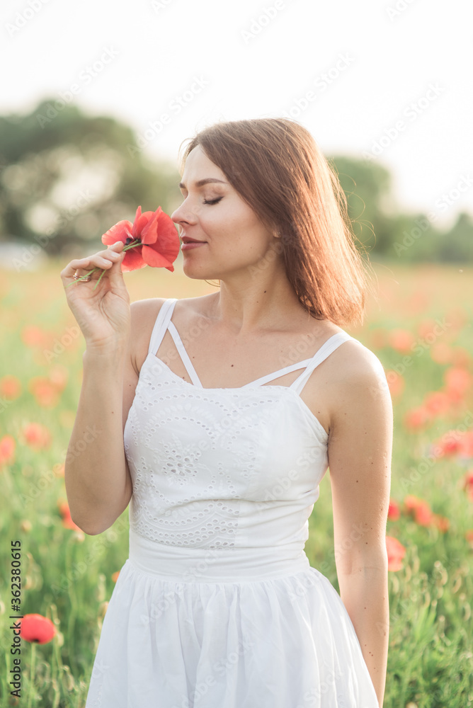 Brunet girl in white dress smelling red flower in a field of poppies. Brunet girl in white dress smelling red flower in a field of poppies.
