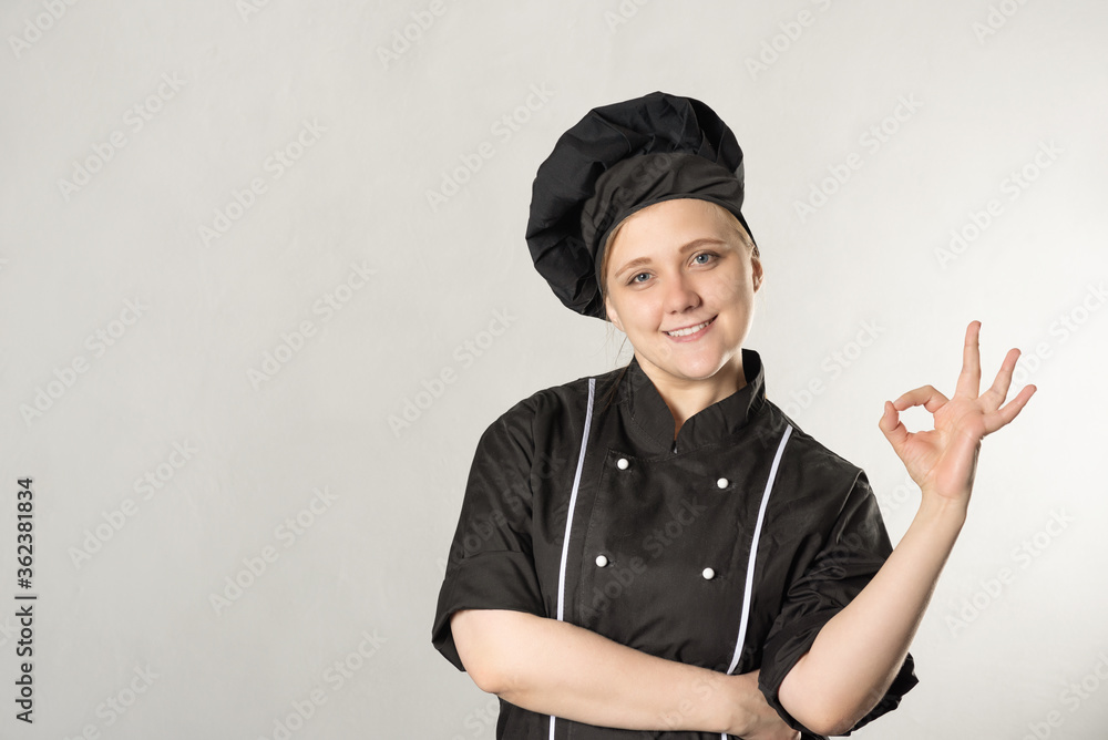 happy woman chef dressed in black uniform on a gray background. cooking concept. shows ok gesture. happy woman chef dressed in black uniform on a gray background. cooking concept. shows ok gesture.