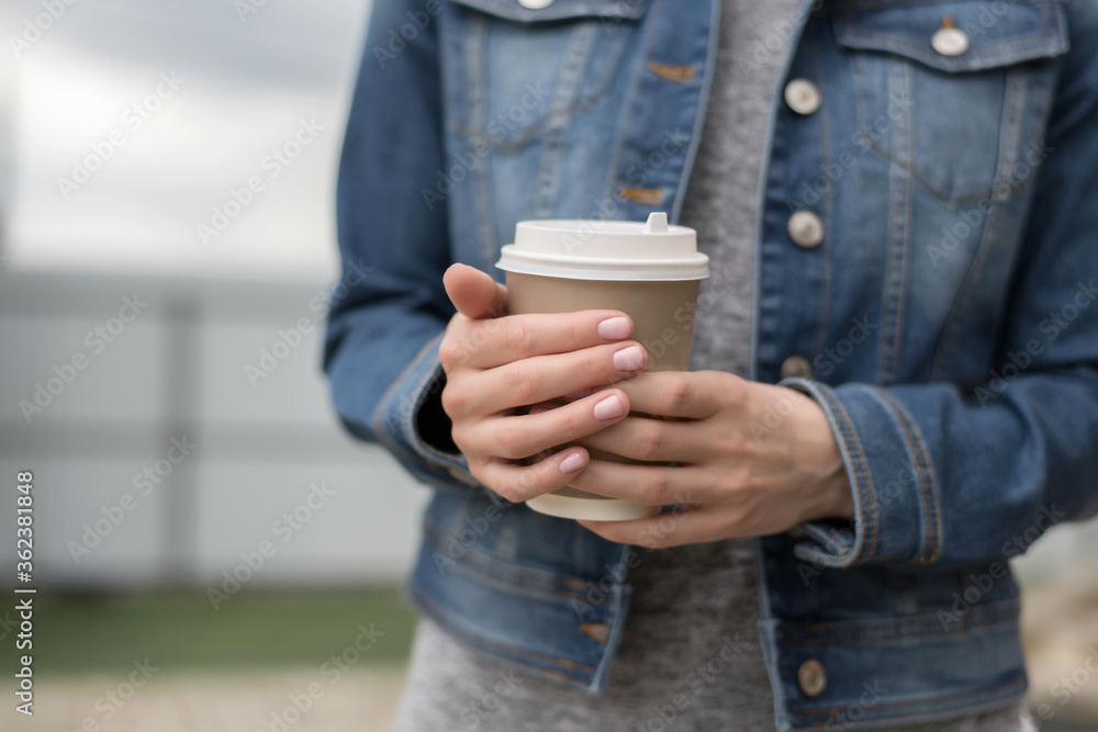 Women's hands in a denim jacket hold a Cup of coffee to go, zero west Women's hands in a denim jacket hold a Cup of coffee to go, zero west