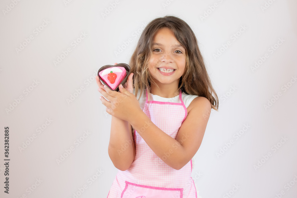 Pretty little girl with a apron on and eating a piece of cake Pretty little girl with a apron on and eating a piece of cake